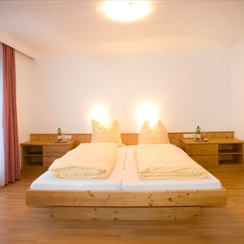 Ein heller Schlafraum mit einem Doppelbett, zwei Nachttischen mit Lampen und einem großen Fenster mit Vorhang.