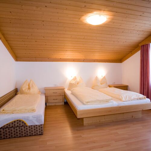 Schlafzimmer mit einem Doppelbett, einem Einzelbett, Nachttischen und einem Fenster mit Vorhängen.